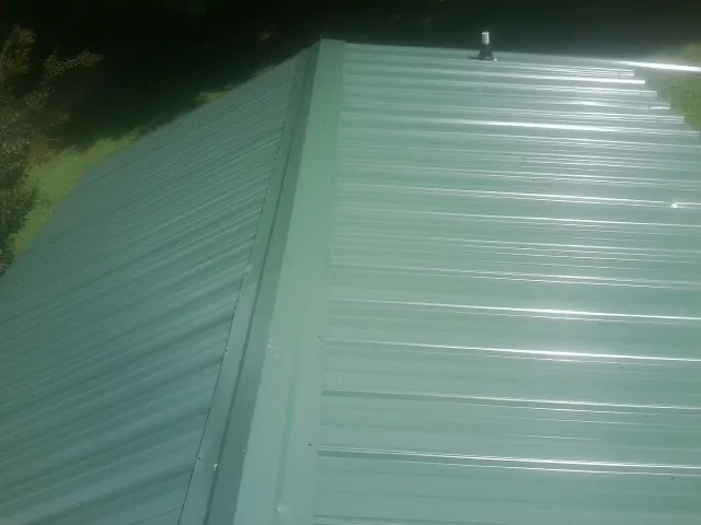 New green metal panels meeting at the ridge of a roof — Flat Roof Repair work by our crew in Plainville